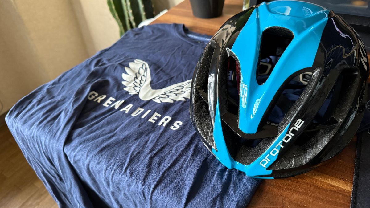 木製テーブルに置かれた青と黒のロードバイク用ヘルメット「KASKプロトーネ」とネイビーのカジュアルなTシャツ。初心者が専用ウェアではなく、気負わない普段着に近い服装で安全にのんびりとソロライドへ出発するための、おすすめの装備コーディネート例。