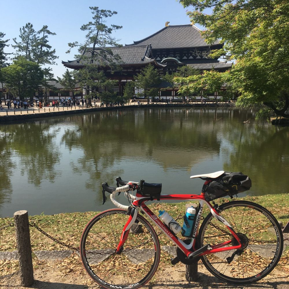 鏡池越しにそびえる東大寺大仏殿を背景に休む、赤と白のロードバイク(ピナレロ)。ダブルボトルやサドルバッグを装備し、初心者が長距離のソロライドへ挑戦する際の安全な準備や持ち物の参考になります。歴史ある奈良の名所を巡るマイペースな自転車旅の記録。