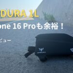 道路脇に置かれた黒いAPIDURAの1Lトップチューブバッグ。「iPhone 16 Proも余裕！本音レビュー」の文字がある。