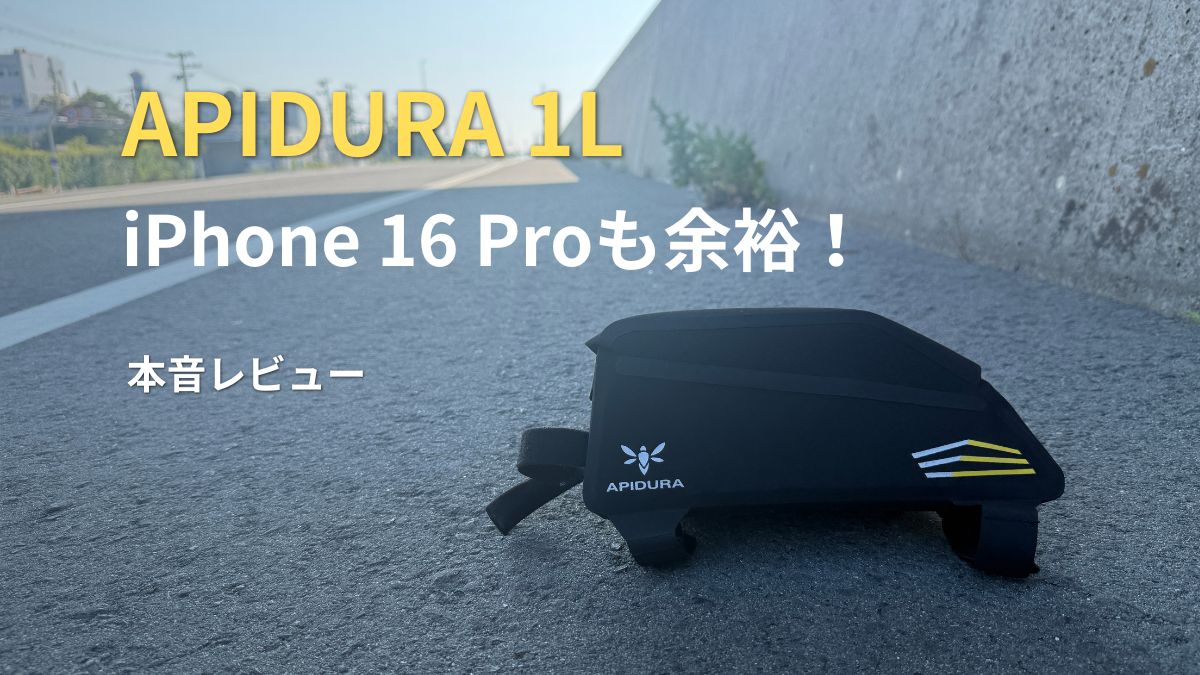 道路脇に置かれた黒いAPIDURAの1Lトップチューブバッグ。「iPhone 16 Proも余裕！本音レビュー」の文字がある。
