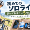 川沿いでロードバイクのサドルバッグを準備する男性サイクリストと、テーブルに並んだスマートフォン、補給食、パンク修理キットなどの必須アイテム。初心者が初めてのソロライドに安心して出かけるための、身軽で安全な持ち物5選を解説するアイキャッチ。